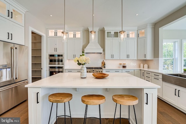 kitchen featuring custom exhaust hood, white cabinetry, stainless steel appliances, and a kitchen island