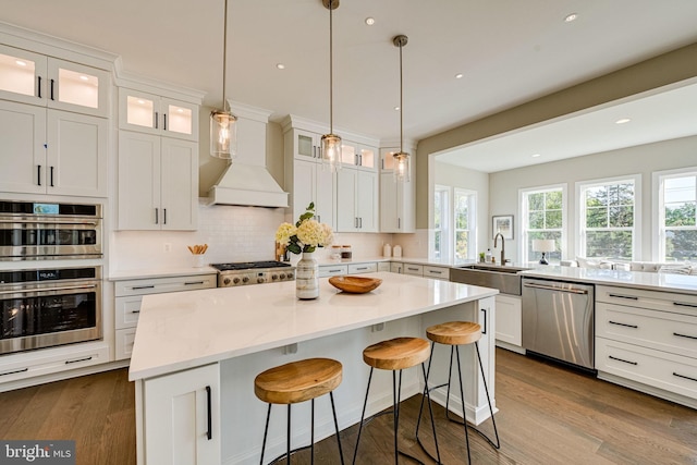 kitchen with white cabinets, a sink, backsplash, custom range hood, and appliances with stainless steel finishes