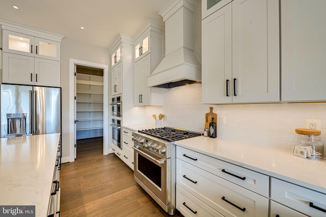 kitchen with high end appliances, decorative backsplash, white cabinetry, and custom range hood