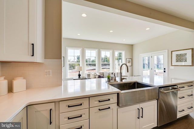 kitchen with dark wood-type flooring, backsplash, sink, stainless steel dishwasher, and white cabinets