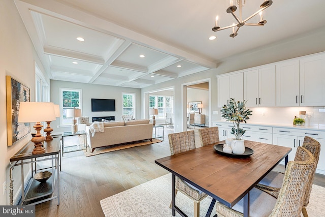 dining area with a notable chandelier, beam ceiling, coffered ceiling, and light wood-type flooring