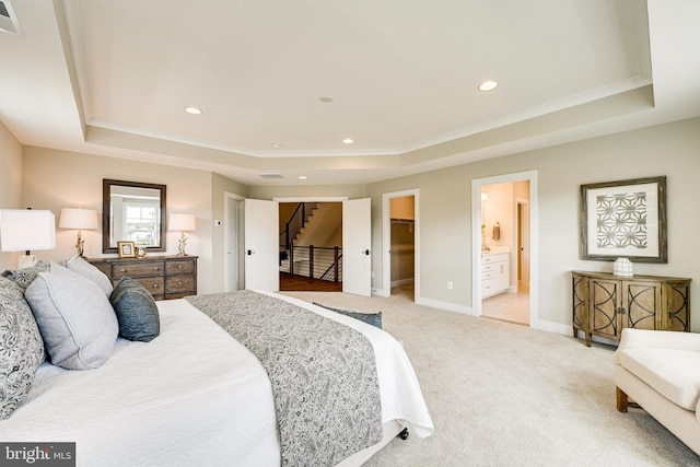 bedroom featuring a spacious closet, a tray ceiling, a closet, connected bathroom, and light colored carpet