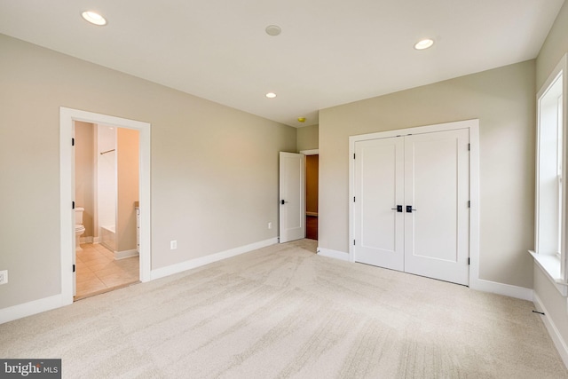 unfurnished bedroom with a closet, light carpet, and ensuite bath