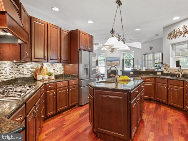 kitchen featuring premium range hood, stainless steel appliances, dark hardwood / wood-style floors, and an island with sink