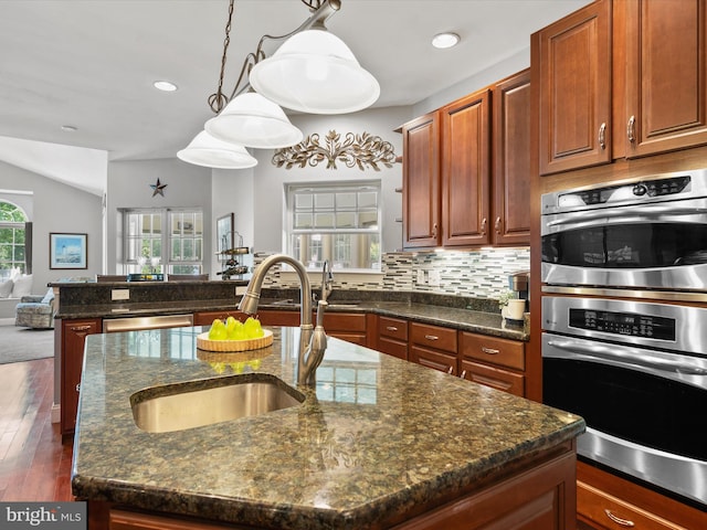 kitchen featuring dark wood-type flooring, stainless steel appliances, a center island with sink, and pendant lighting