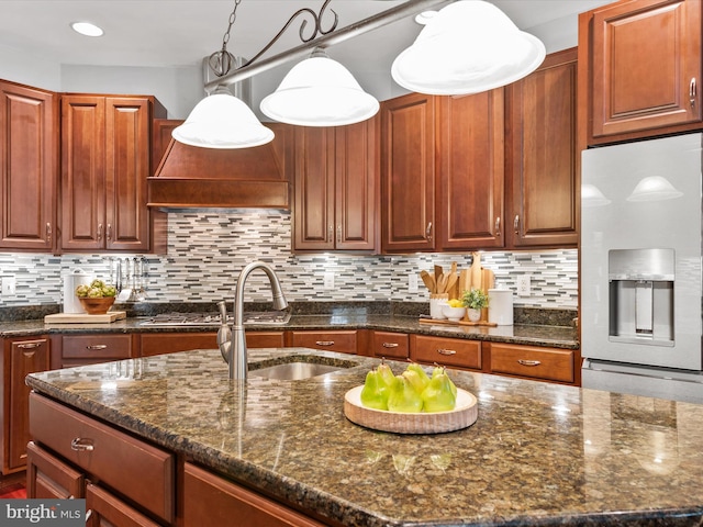 kitchen with fridge with ice dispenser, sink, dark stone counters, and pendant lighting