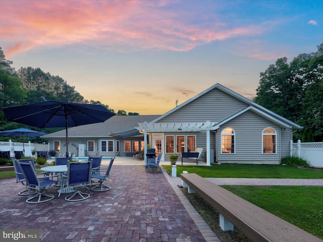 back house at dusk featuring a pergola, a patio area, and a lawn