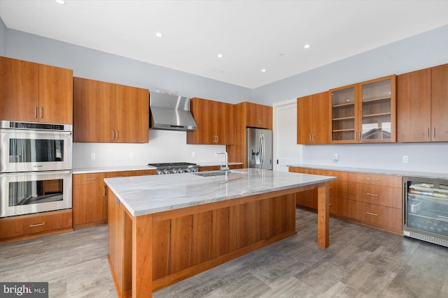 kitchen featuring wall chimney range hood, wood-type flooring, a center island with sink, sink, and appliances with stainless steel finishes