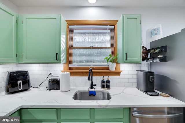 kitchen with green cabinets, sink, light stone counters, and backsplash