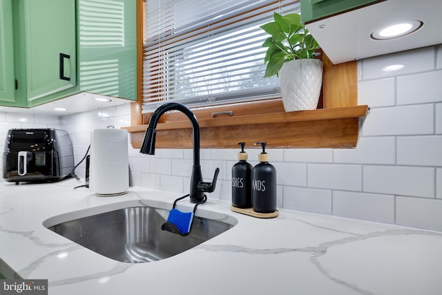 room details featuring decorative backsplash, green cabinets, and light stone counters