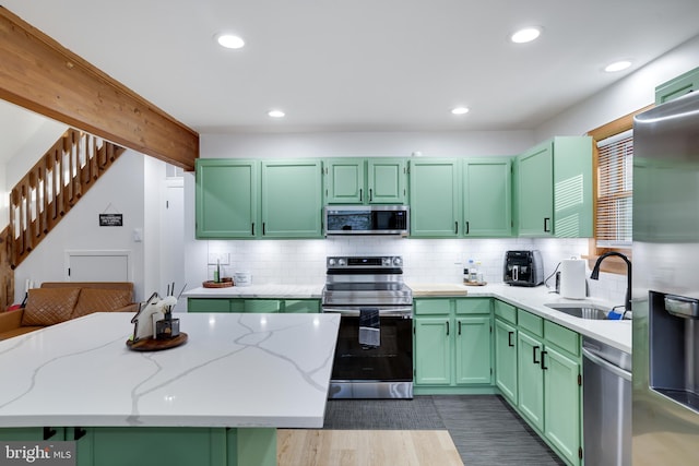 kitchen featuring decorative backsplash, stainless steel appliances, sink, green cabinetry, and light stone counters