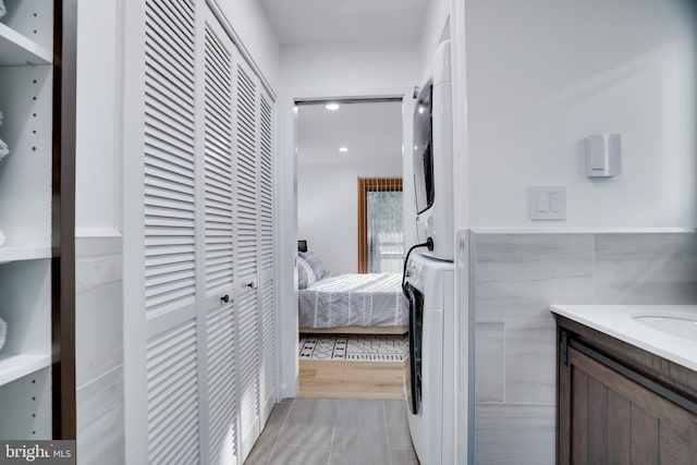 hallway with tile walls, light hardwood / wood-style flooring, and stacked washing maching and dryer