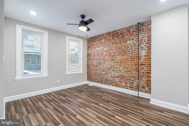 unfurnished room featuring brick wall, dark wood-type flooring, and ceiling fan