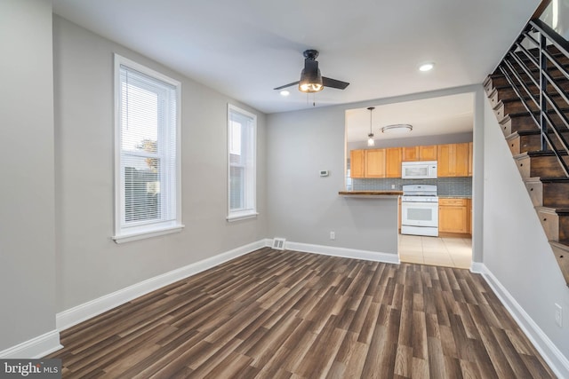 unfurnished living room featuring dark wood-type flooring and ceiling fan