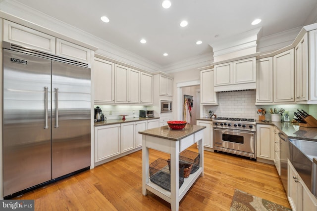 kitchen featuring built in appliances, light hardwood / wood-style floors, ornamental molding, tasteful backsplash, and white cabinets