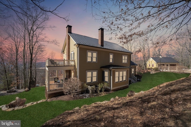 back house at dusk with a lawn, a deck, and a balcony