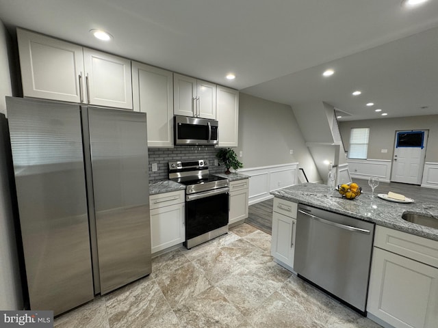 kitchen with light stone countertops, appliances with stainless steel finishes, backsplash, and white cabinetry