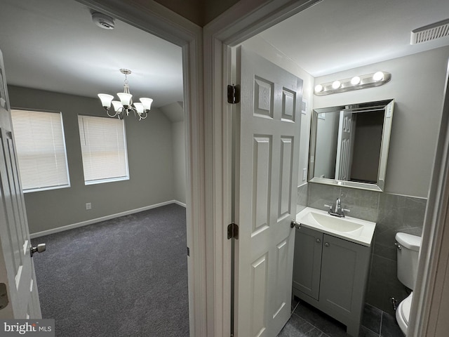 bathroom with toilet, vanity, tile walls, and an inviting chandelier