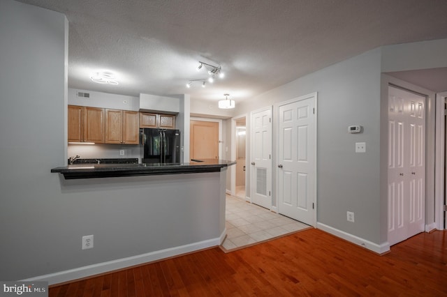 kitchen featuring a textured ceiling, light hardwood / wood-style flooring, kitchen peninsula, and black refrigerator