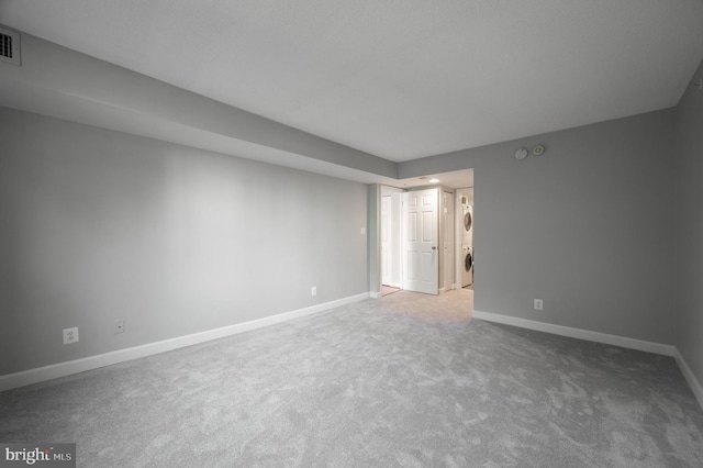 carpeted empty room with baseboards and stacked washer / dryer