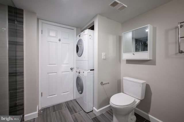 bathroom with toilet, wood tiled floor, stacked washing maching and dryer, baseboards, and visible vents
