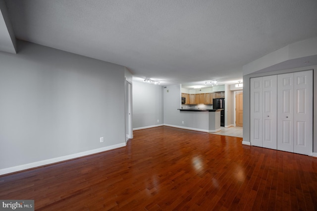 unfurnished living room featuring baseboards, wood finished floors, and a textured ceiling