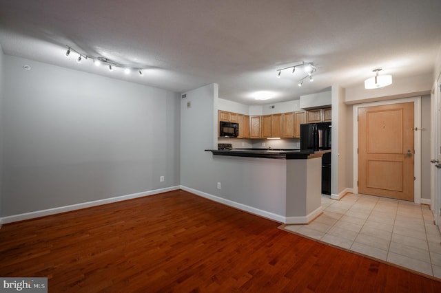 kitchen with light hardwood / wood-style flooring, kitchen peninsula, a textured ceiling, and black appliances