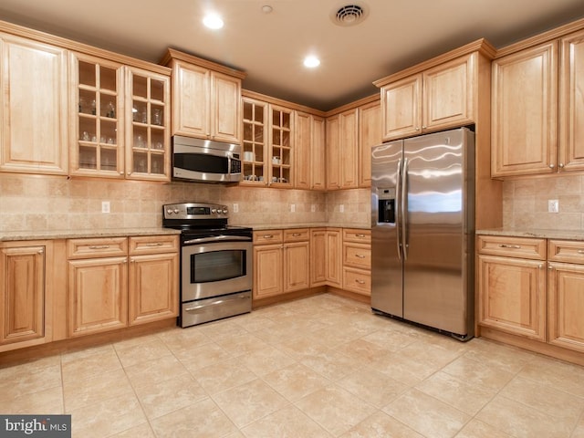 kitchen featuring light stone counters, stainless steel appliances, tasteful backsplash, and light brown cabinets