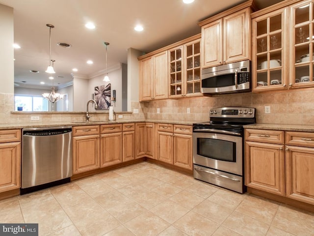 kitchen with hanging light fixtures, appliances with stainless steel finishes, light stone counters, and ornamental molding