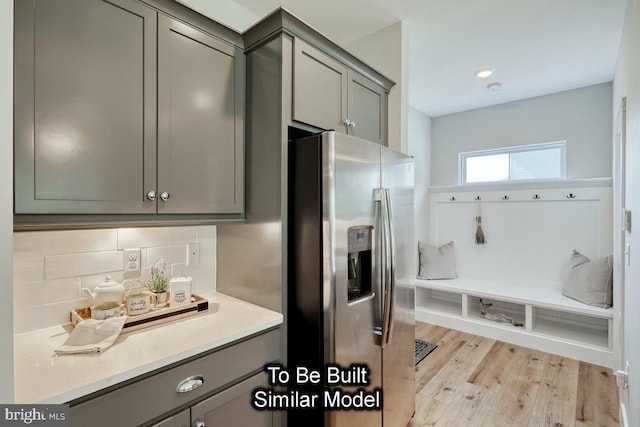 kitchen with gray cabinets, backsplash, light wood-type flooring, and stainless steel fridge with ice dispenser