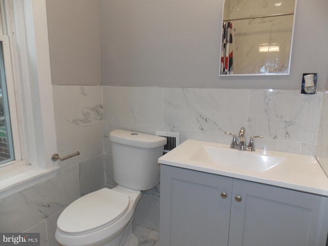 bathroom with vanity, toilet, and tile walls