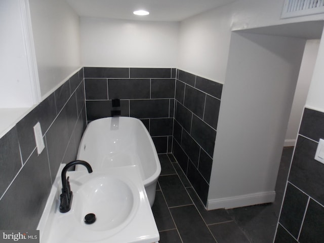 bathroom featuring tile walls, tile patterned flooring, a tub to relax in, and sink