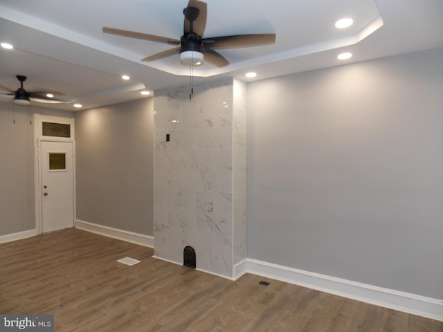 empty room with wood-type flooring, ceiling fan, and a raised ceiling