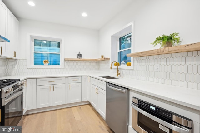 kitchen with sink, appliances with stainless steel finishes, light hardwood / wood-style flooring, and white cabinets