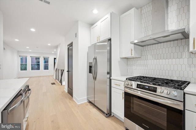 kitchen featuring white cabinets, wall chimney range hood, stainless steel appliances, and light wood-type flooring