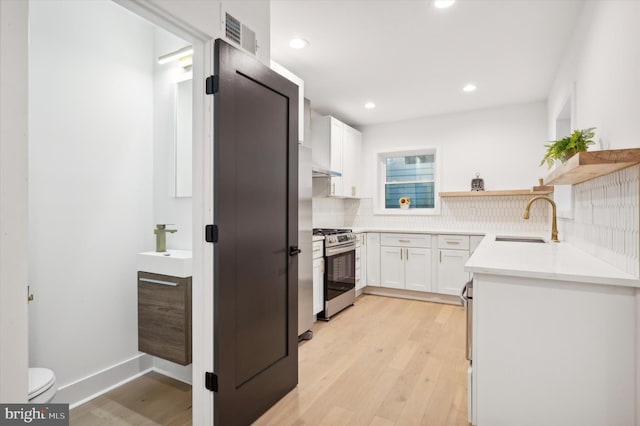 kitchen with backsplash, sink, light wood-type flooring, stainless steel range with gas cooktop, and white cabinetry