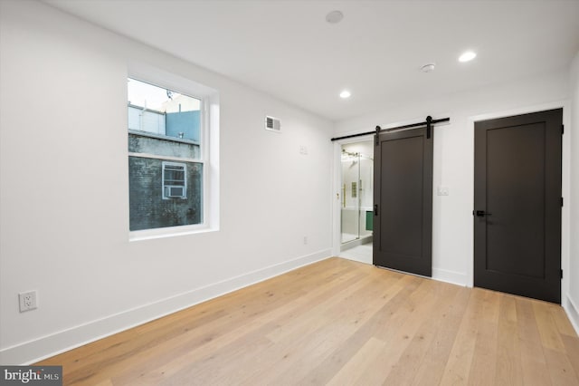 unfurnished bedroom with light wood-type flooring and a barn door