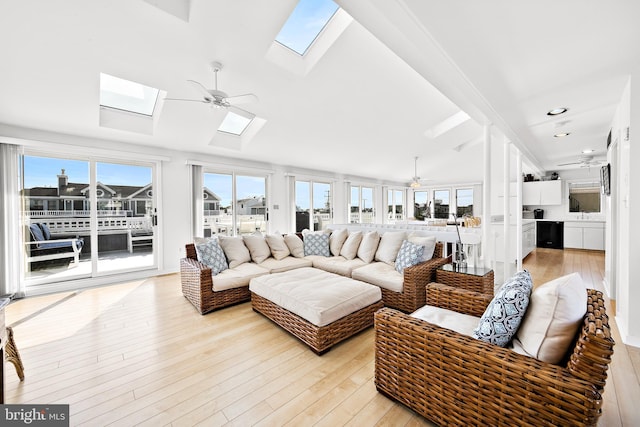 living area with vaulted ceiling with skylight, light wood finished floors, and ceiling fan