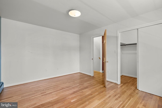 unfurnished bedroom featuring a closet, light hardwood / wood-style floors, and a baseboard heating unit