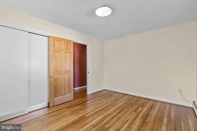 unfurnished bedroom featuring a closet, a baseboard heating unit, and hardwood / wood-style flooring