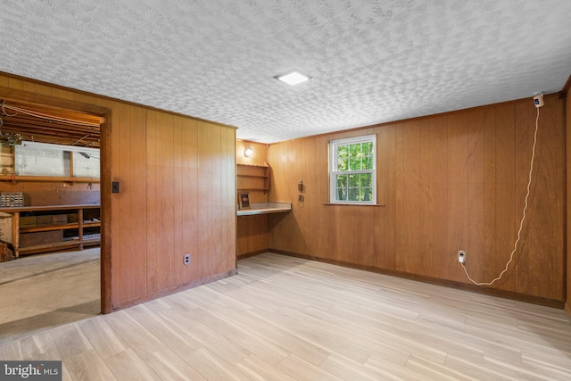 unfurnished living room with a textured ceiling, light wood-type flooring, and wood walls