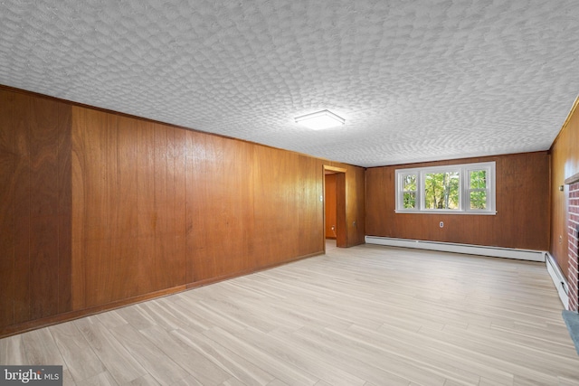 spare room with wood walls, a textured ceiling, light hardwood / wood-style flooring, and baseboard heating