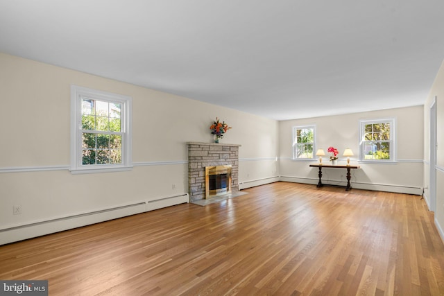 unfurnished living room with a baseboard heating unit, a stone fireplace, wood-type flooring, and a healthy amount of sunlight