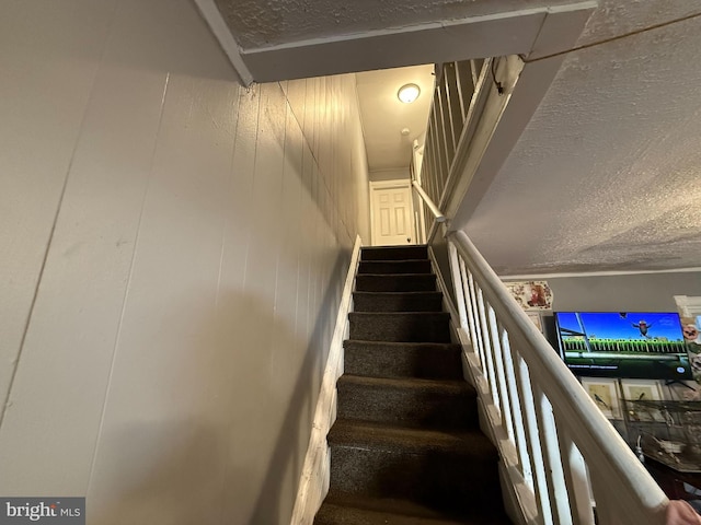 stairway with wood walls and a textured ceiling