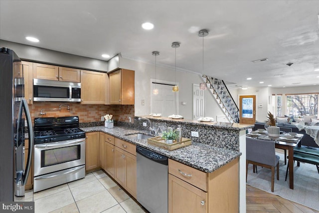 kitchen with kitchen peninsula, dark stone countertops, stainless steel appliances, sink, and decorative light fixtures