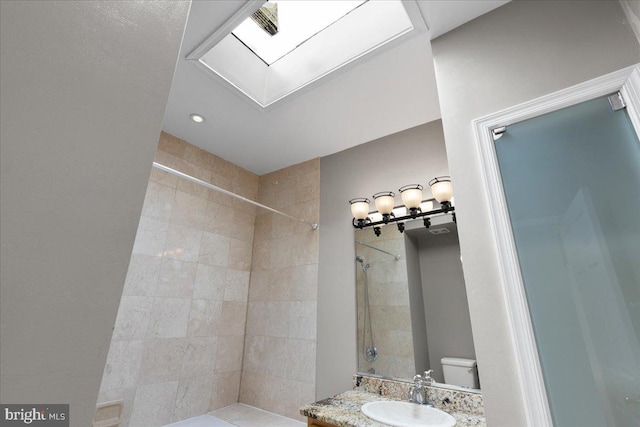 bathroom featuring vanity, tiled shower, toilet, and a skylight