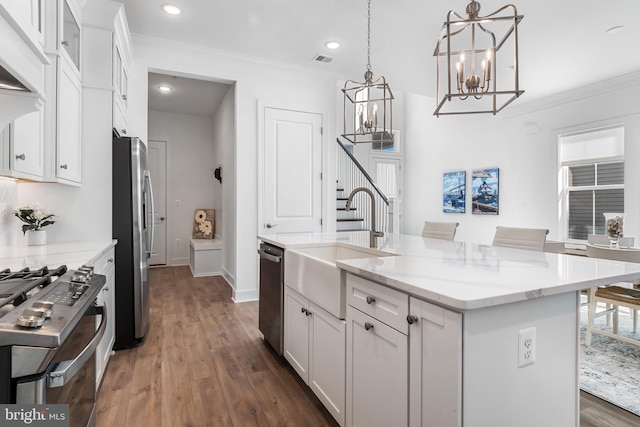 kitchen featuring a center island with sink, white cabinetry, stainless steel appliances, decorative light fixtures, and dark hardwood / wood-style floors