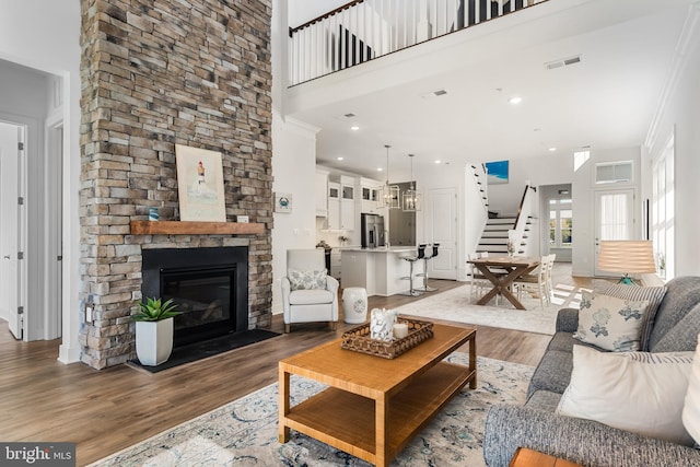 living room featuring a high ceiling, a stone fireplace, hardwood / wood-style flooring, crown molding, and an inviting chandelier