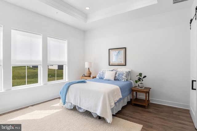 bedroom featuring dark hardwood / wood-style floors, a barn door, and a raised ceiling