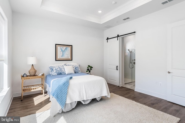 bedroom with a barn door, wood-type flooring, and a tray ceiling